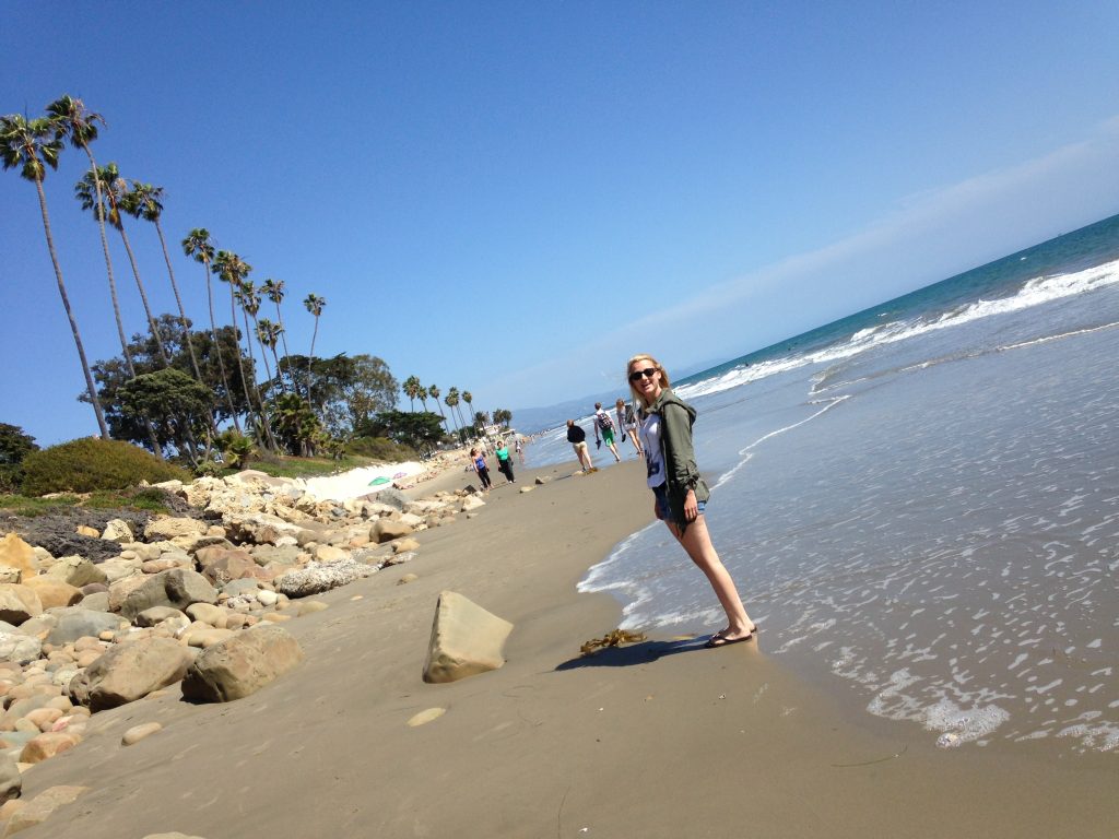 Woman standing at Butterfly Beach in Santa Barbara with palm trees and ocean waves