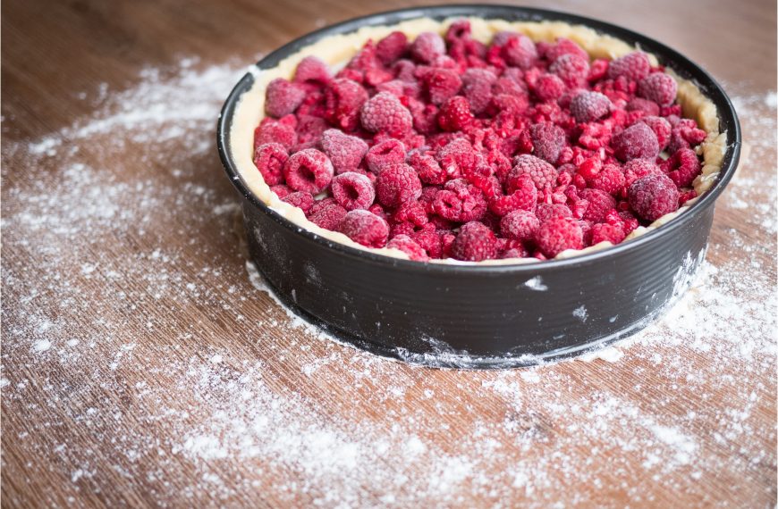 Unbaked raspberry cake filled with fresh raspberries in a baking tin on a wooden surface