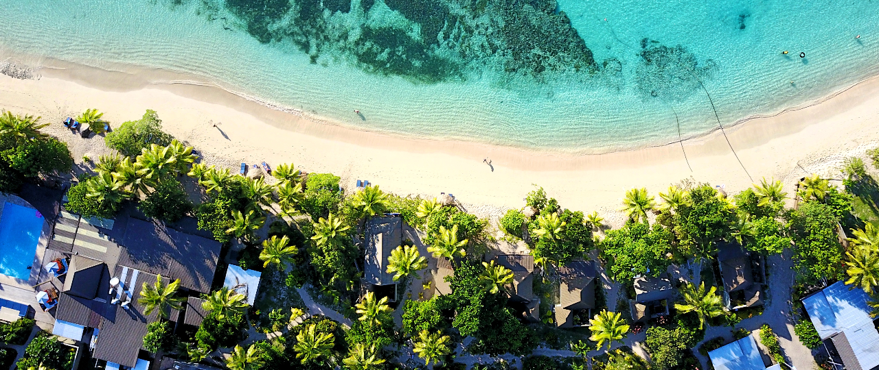 Aerial view of a tropical lagoon in Fiji with turquoise water, a white sandy beach, and palm trees.
